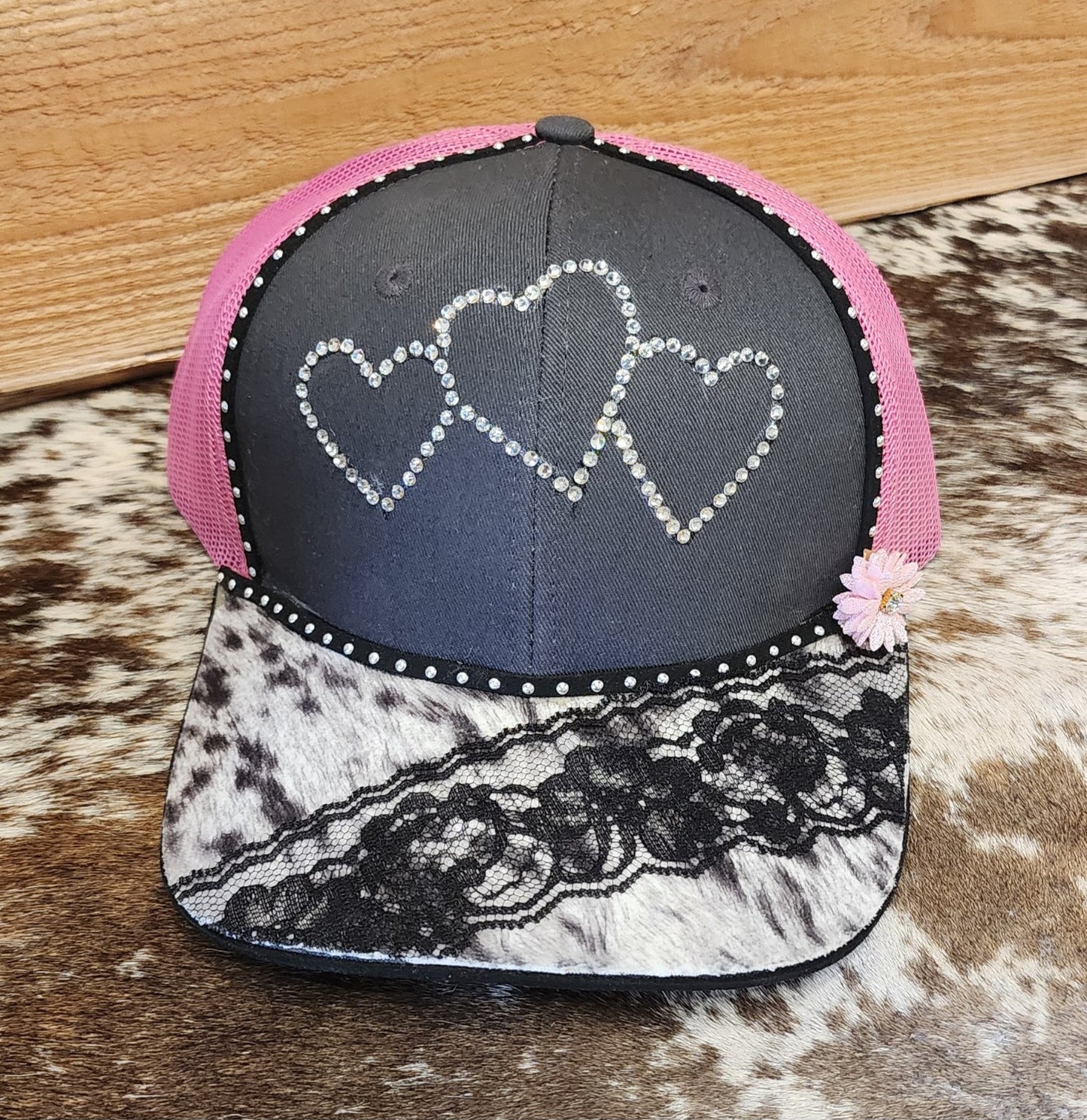One-of-a-kind handcrafted snapback with three rhinestone hearts, pink mesh, cowhide-patterned bill and black lace